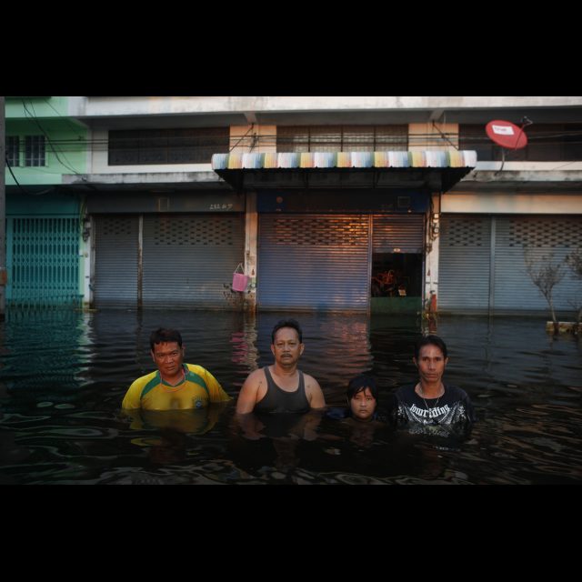Samran Pannarat, Wanchai Palagawong, Tanee Yoo Suksawan (girl) and Tanicha Songbangjak pause to be photographed while walking through the chest high floodwaters in Amornchai Village, on the outskirts of Bangkok. This is the start of the huge tract of water which is encircling the city. The outer regions of Bangkok have endured rising floodwaters over the past two weeks as the floodwaters which have inundated large parts of the country move through towards the sea. Thailand is experiencing the worst flooding in over 50 years which has affected more than nine million people.<br>
Image by © Gideon Mendel/Corbis
