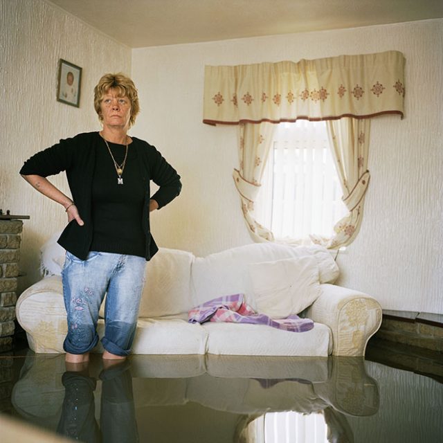Margaret Clegg is shocked as she surveys the floodwaters and the damage inside her home in Toll Bar village outside Doncaster. She had only recently put down a new floor in her kitchen, new carpets, installed new doors and purchased her new lounge suite. She owns her house and does have insurance cover. On the previous Monday she went to bed and woke up in the morning to find the water half way up her kitchen. 'I feel awful I could cry'. There is nothing I can do about it, I just have to carry on'. This was one of the communities flooded when a freak storm unleashed a deluge of rain on parts of northern England in which more than four inches of rain fell in 24 hours. The devastation was caused by extreme and unpredictable weather and it is this kind of freak event, which climate scientists have been predicting, will become more frequent as a consequence of global warming.<br>
Chromogenic print on Fuji Crystal Archive<br>
27 1/2” x 27 1/2 / 48” x 48”; Edition: 5 + 2 AP
<br>
70 x 70 cm / 122 x 122 cm; Edition: 3 + 2 AP