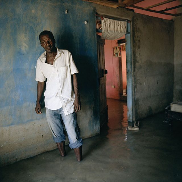 Tibo Jean Fritzner, 48, faces the camera in his flooded home in Decade in southeast Haiti. His house was damaged by Hurricane Gustav. During the hurricane season of 2008 Haiti was subjected to four destructive hurricanes in the space of twenty days. This increasing severity and quantity of hurricanes is one of the effects of climate change. “We were very scared when the hurricane came. It was very windy and there were corrugated iron sheets flapping noisily. There was so much noise – the wind, and people crying, people shouting and running in the street. Someone came to help my mother get away, and someone else helped me with the pigs and goats. So then we left the house and fled. We had no idea whether the house would still be there afterwards – we just saved ourselves. This is the highest the water has ever risen. I’ve never seen a flood like it.”<br>
Chromogenic print on Fuji Crystal Archive<br>
27 1/2” x 27 1/2 / 48” x 48”; Edition: 5 + 2 AP
<br>
70 x 70 cm / 122 x 122 cm; Edition: 3 + 2 AP