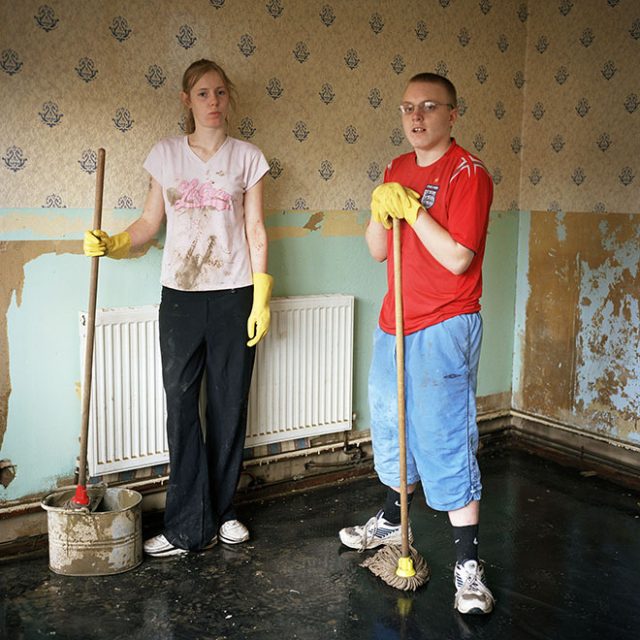 Carrie-Ann Garner and Danny Jones pose for a photograph as they try to sweep the last of the floodwater out of the house in Toll Bar village that Danny shares with his mother. Carrie Ann is a neighbour who was helping out. In the background the level that the floodwaters came up to is visible, as the wallpaper is peeled off up to that height. This was one of the communities flooded when a freak storm unleashed a deluge of rain on parts of northern England in which more than four inches of rain fell in 24 hours. The devastation was caused by extreme and unpredictable weather and it is this kind of freak event, which climate scientists have been predicting, will become more frequent as a consequence of global warming