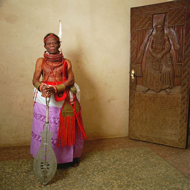 The Ayobahan is the fourth-ranking chief in Iwebo, the palace society responsible for care of the king’s ritual regalia. He holds the eben, the ceremonial sword, and wears a finger-pattern hanging garment, a gift from the Oba, emblem of self-achieved prosperity.
Series: <i>Kings, Chiefs, and Women of Power</i><br>
Chromogenic print on Fujiflex Crystal Archive paper<br>
30” x 30”; Edition: 5 + 2 AP<br>
50” x 50”; Edition: 3 + 1 AP