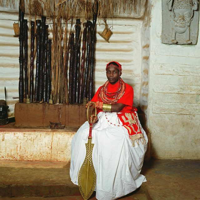Chief Nosahare is chief priest of the shrines to the departed kings and keeper of the king’s ancestral staffs. As custodian of the king’s ancestors, he blesses the king’s head, seat of judgment and character on which welfare of the people depends. Wearing coral beads, brass bracelet and a flaglike adornment hanging at his side, he sits in front of the shrine holding staffs dedicated to his own paternal ancestors.,<br>
Series: <i>Kings, Chiefs, and Women of Power</i><br>
Chromogenic print on Fujiflex Crystal Archive paper<br>
30” x 30”; Edition: 5 + 2 AP<br>
50” x 50”; Edition: 3 + 1 AP