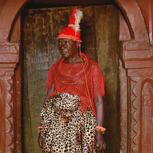 His red, coral-beaded attire marks the importance of the Olihga, senior member of the Uzama, the high-ranking chiefs known as kingmakers. As the person who crowns the king, the Olihga alone does not kneel before him. While his leopard-patterned wrapper is probably worn for style, the leopard is a totem of the king, and war captains formerly wore leopard-embroidered tunics as emblems of loyalty.<br>
Series: <i>Kings, Chiefs, and Women of Power</i><br>
Chromogenic print on Fujiflex Crystal Archive paper<br>
30” x 30”; Edition: 5 + 2 AP<br>
50” x 50”; Edition: 3 + 1 AP