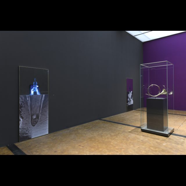 Installation view. <i> Hunting horn with scarifications by the coppersmith Guido Clabots, Dinant, Belgium, </i> copper. <br> Mirror works with <i> photo of Hans Himmelheber and X-ray tomography of a power figure acquired by him</i>, 2019.<br> Commissioned by the Rietberg Museum, Zurich for the exhibition <i>Congo as Fiction</i>. <br> photo: Rainer Wolfsberger